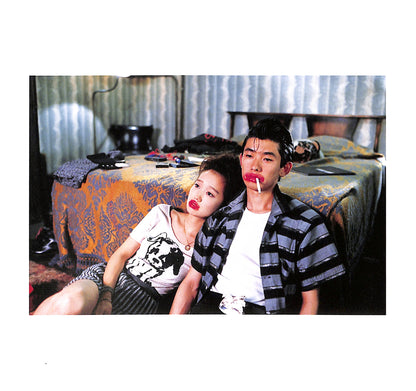 Internal page - JIM JARMUSCH & MASAYOSHI SUKITA / MYSTERY TRAIN. Two people sitting on a bed in a room with various items around.
