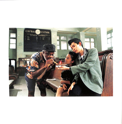 Internal page - JIM JARMUSCH & MASAYOSHI SUKITA / MYSTERY TRAIN. Three people sitting together in a train station with a large clock in the background.