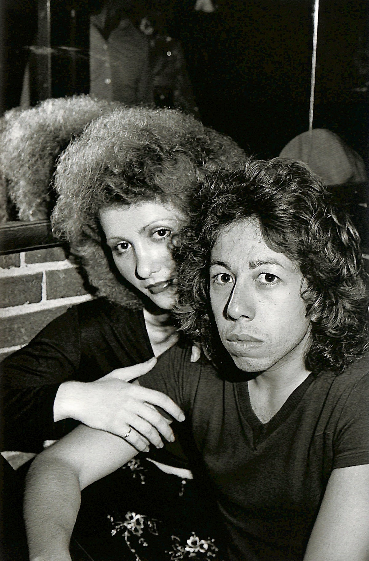 Interior image - NAN GOLDIN / COUPLES AND LONELINESS. Two people with curly hair sitting close together in a black and white photo.
