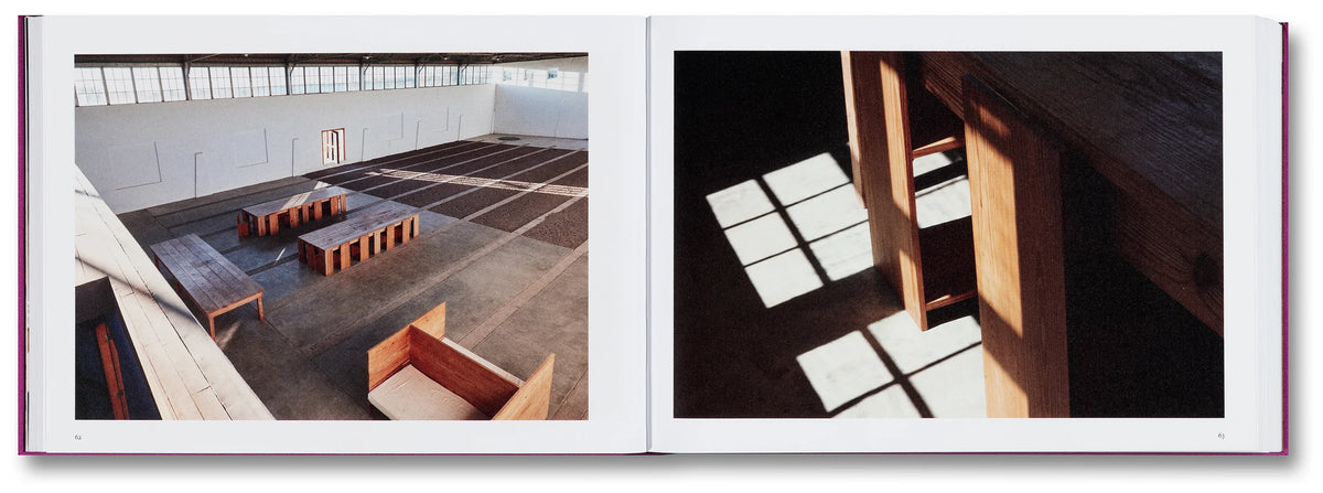 Interior shot of  an Open book showing two architectural photographs: one of a large open space with tables and chairs, the other of a wooden structure with square panels.